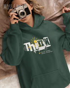 frau trägt streetwear hoodie im oversize fit in farbe moss green mit think motiv auf der Brust