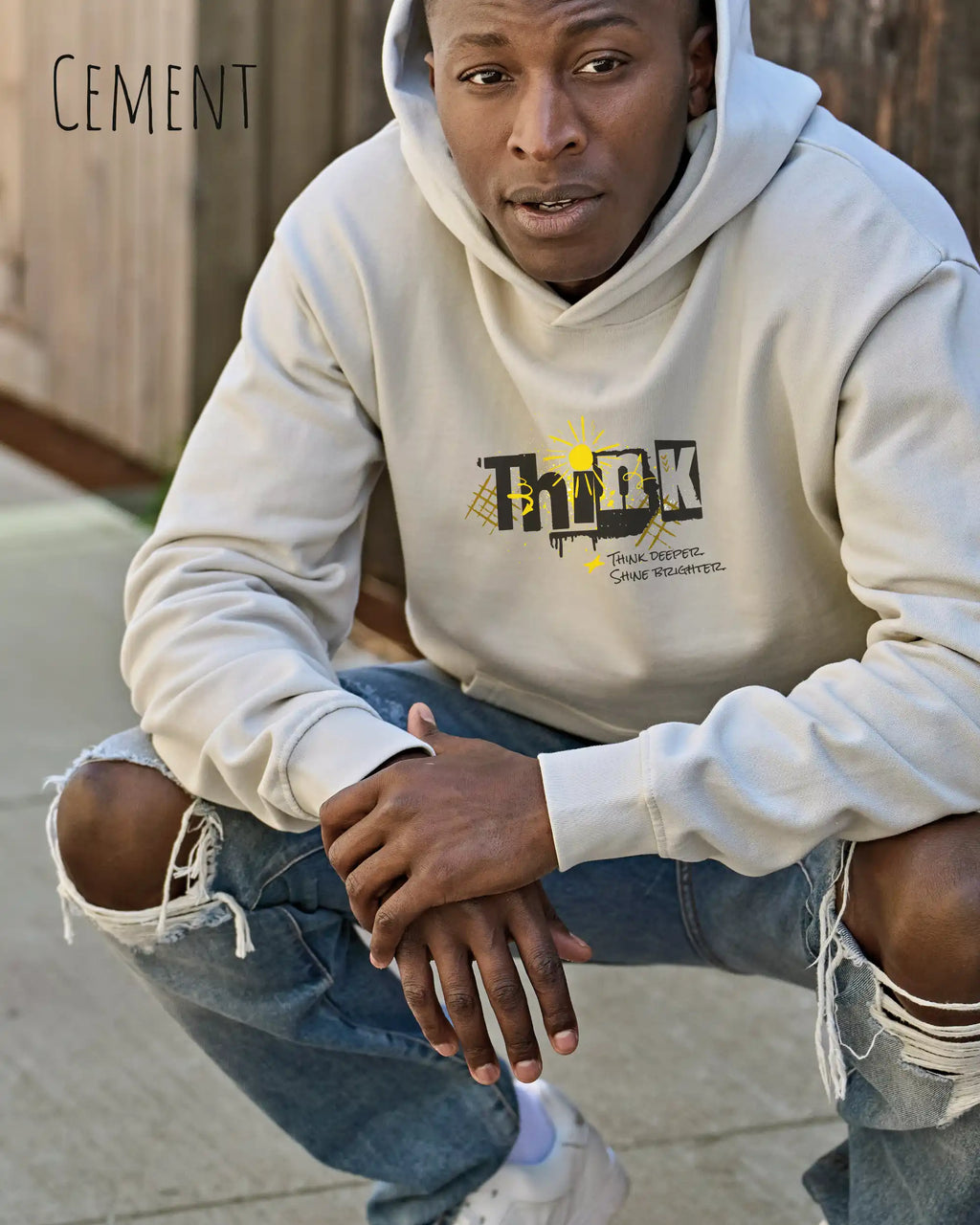 Ein Mann trägt das Tee Jays Heavy Loose Fit Hooded Sweatshirt 5162 in der Farbe Cement Mut dem Statement Design THINK.