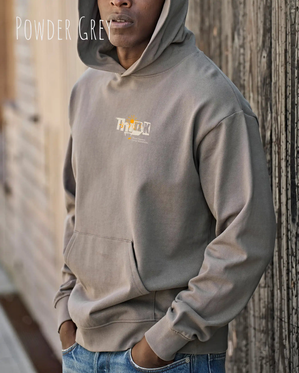 Mann trägt das Tee Jays Heavy Loose Fit Hooded Sweatshirt 5162 in der Farbe powere grey mit dem Statement Design THINK links oben auf der Brust.