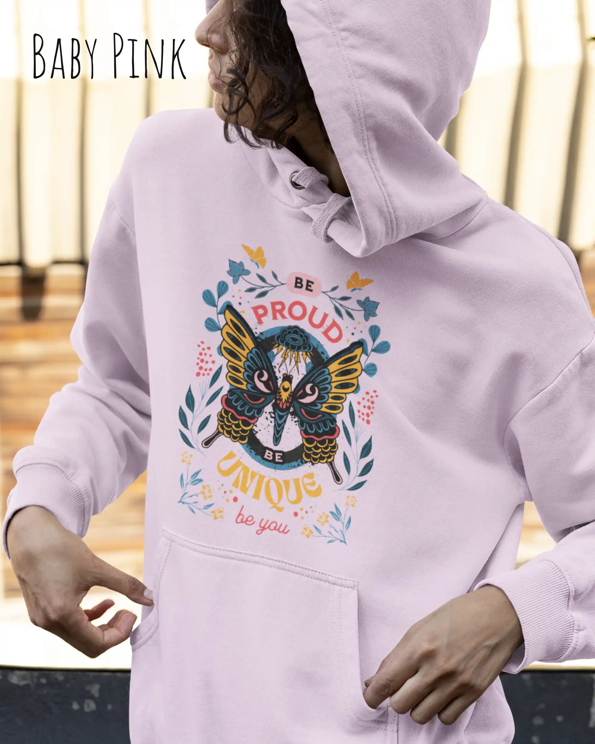 Frau trägt hoodie im feminine fit aus weicher baumwollmischung in farbe baby pink mit be proud motiv auf der Brust