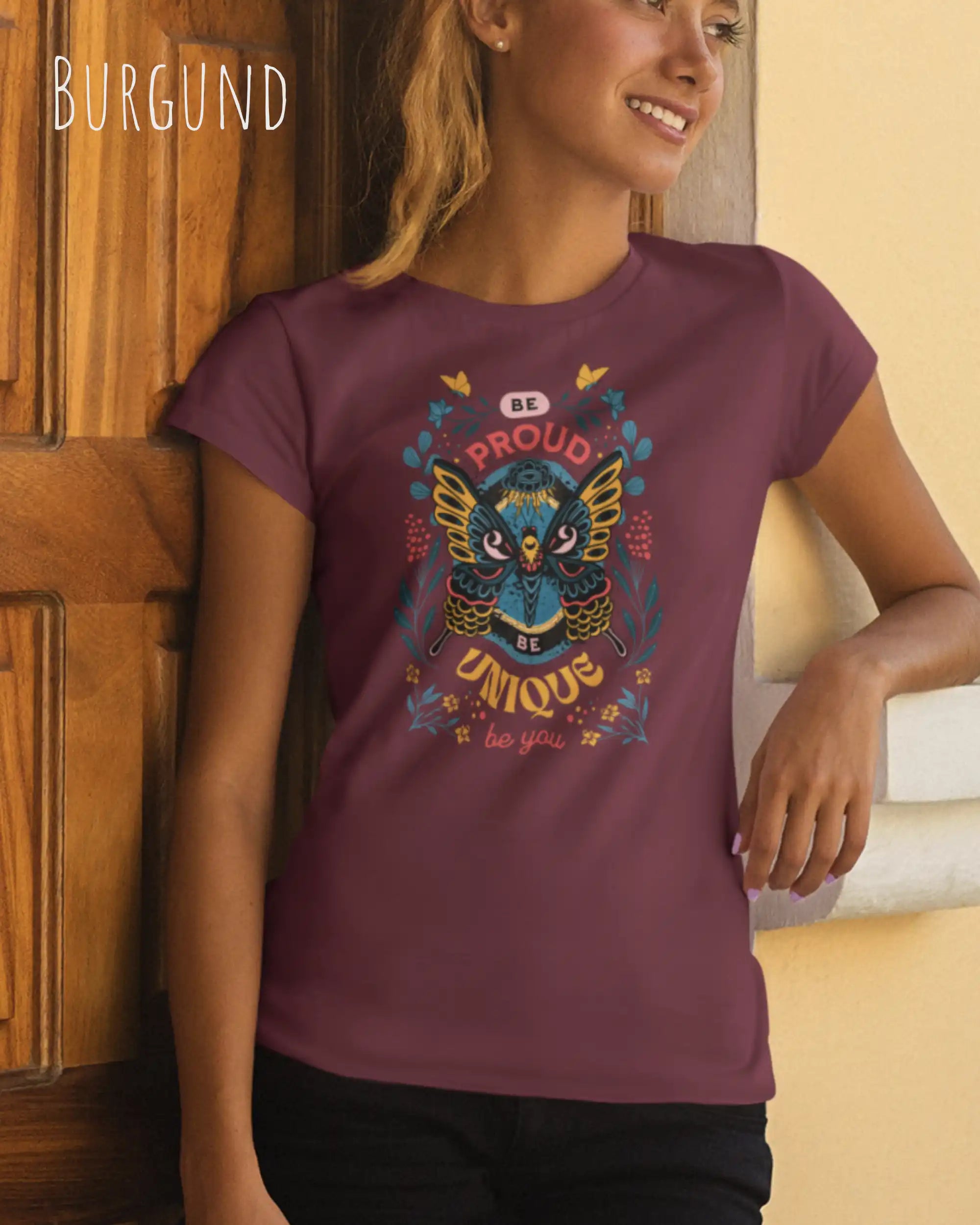 Eine Bonde Frau trägt das Basic Design T-Shirt feminine fit in der farbe burgund mit dem statement Be proud be you