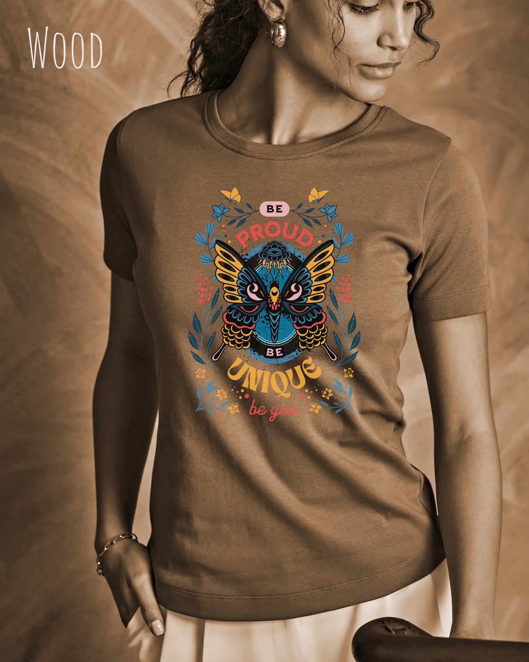 Das Bild zeigt eine frau, die ein design-t-shirt in der farbe wood mit der boho-Grafik be proud trägt.