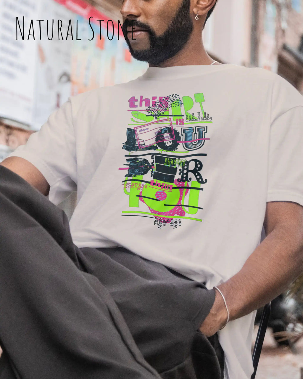 Mann im Strassemcafe  trägt das Heavyweight Oversized T-Shirt AWDis 240 T in der Farbe natural stone  mit dem Design LOUDER auf der Brust.