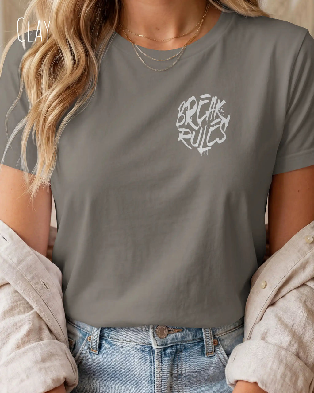 Eine blonde frau trägt ein design t-shirt mit femininem schnitt in der farbe clay und mit der grafik "break rules" oben links.