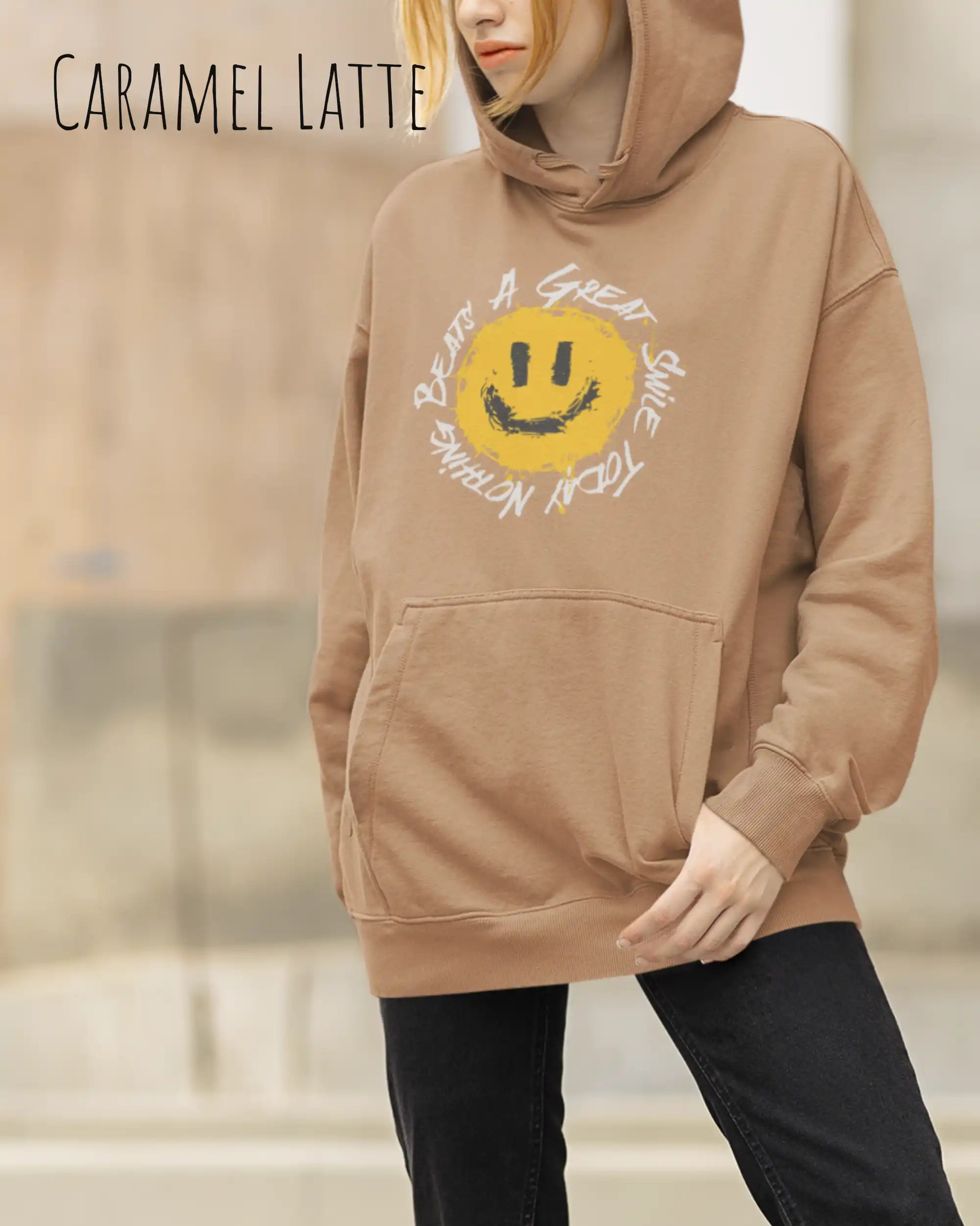 Das Bild zeigt eine Frau, die einen Design-Hoodie in der Farbe caramel latte und mit der Grafik Nothing beats a great smile trägt.