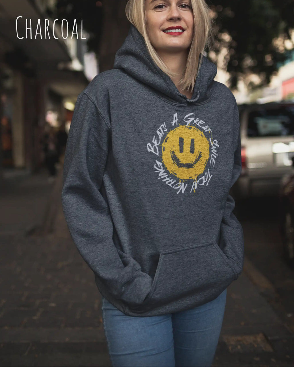 Das Bild zeigt eine blonde Frau, die einen Design-Hoodie in der Farbe charcoal und mit der Grafik Nothing beats a great smile trägt.