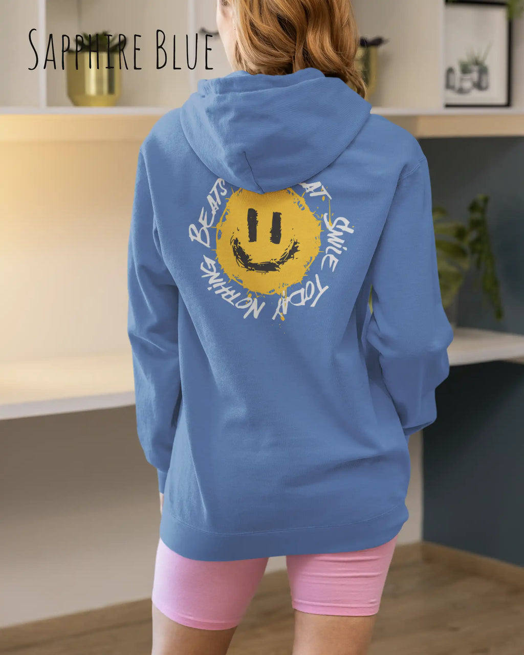 Das Bild zeigt eine Frau, die einen Design-Hoodie in der Farbe sapphire blue und mit der backprint Grafik Nothing beats a great smile trägt.