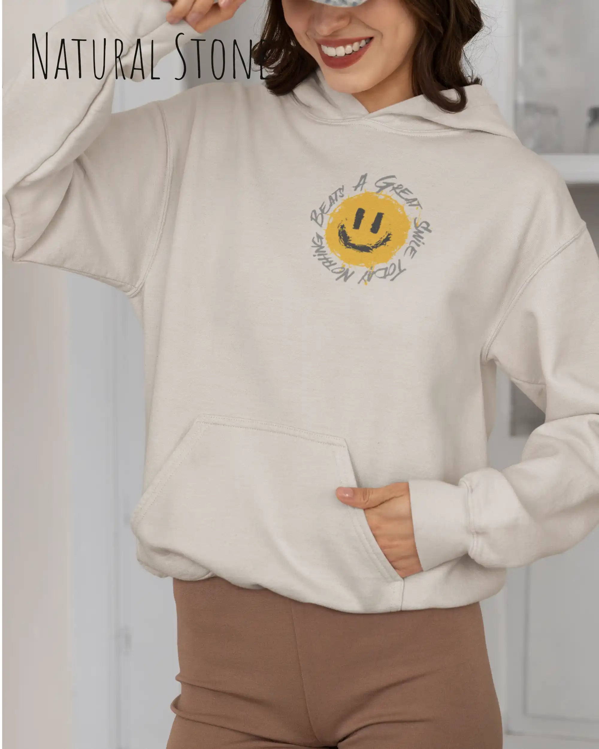 Das Bild zeigt eine frau, die einen  oversized Grafik hoodie in der farbe natural stone mit dem design notihing beats a great smile trägt.