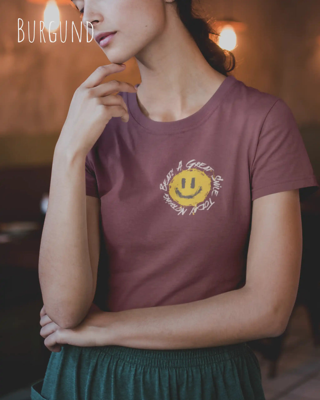 Junge Frau trägt ein Design-T‑Shirt im Feminine Fit in der Farbe Burgund. Das Design zeigt das Statement NOTHING BEATS A SMILE.