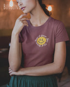 Junge Frau trägt ein Design-T‑Shirt im Feminine Fit in der Farbe Burgund. Das Design zeigt das Statement NOTHING BEATS A SMILE.