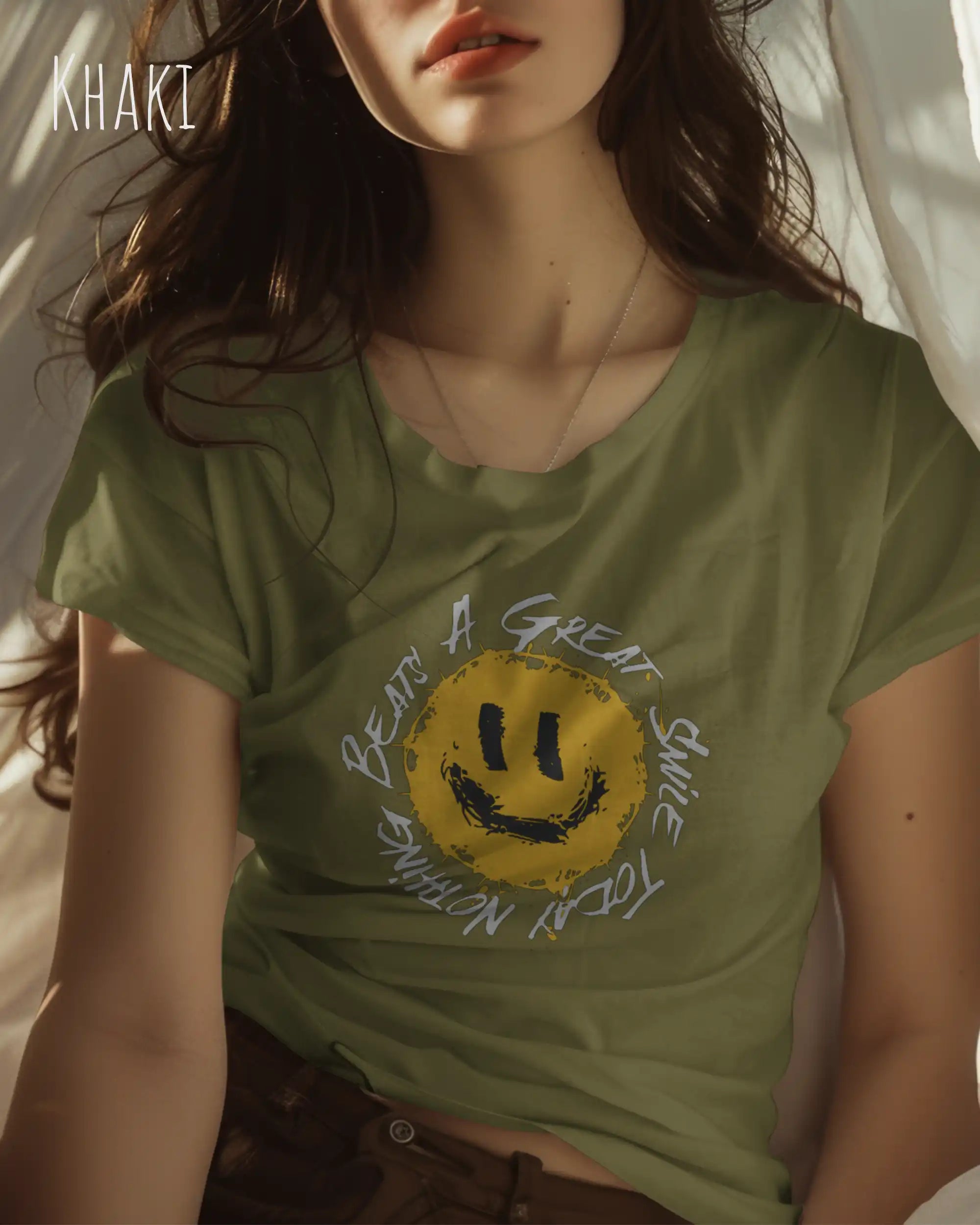 Junge Frau trägt ein Design-T‑Shirt im Feminine Fit in der Farbe khaki. Das Design zeigt das Statement NOTHING BEATS A SMILE und ist vorne auf der Brust gedruckt.