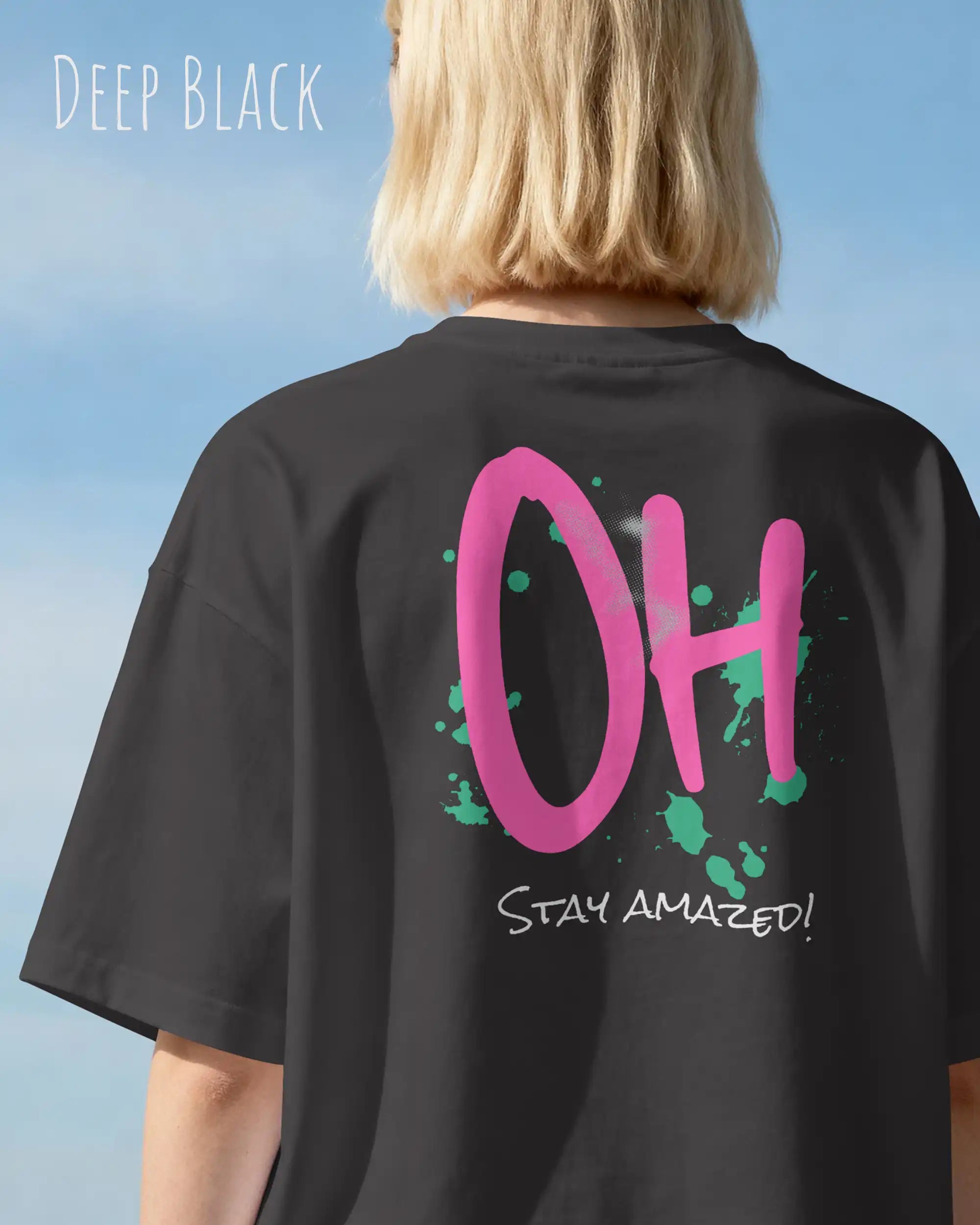 Frau trägt das Heavyweight Oversized T-Shirt AWDis 240 T in der Farbe deep black mit dem Design OH STAY AMAZED auf dem Rücken.