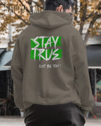 das bild zeigt einen mann, der einen Oversized Design-Hoodie in der farbe natural clay mit dem ausdrucksstarken backprint "stay true ... just be you" trägt.