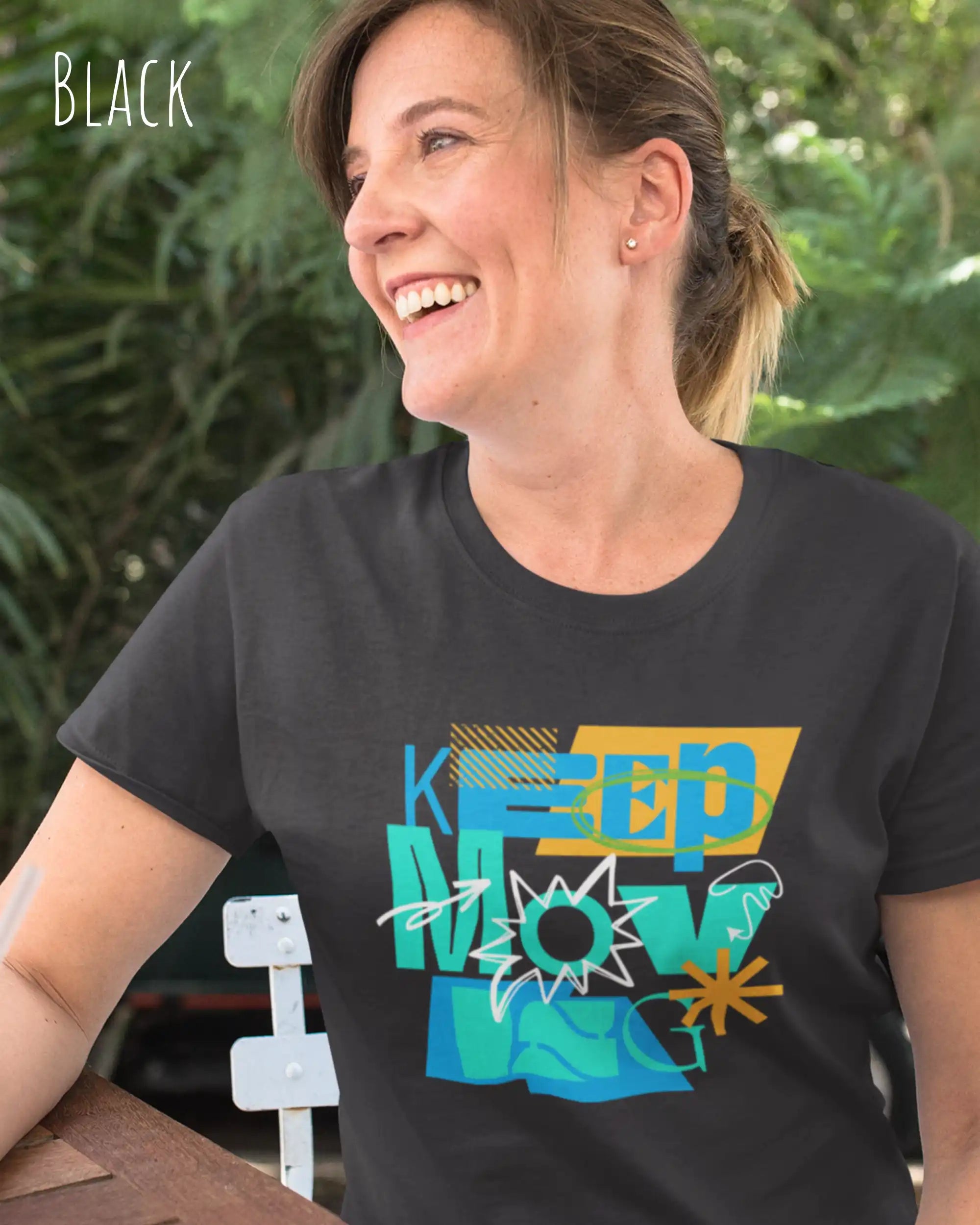 Dieses Bild zeigt eine lachende frau, die ein feminines design-T-Shirt in der farbe black und mit der motivierenden grafik "keep moving" trägt.