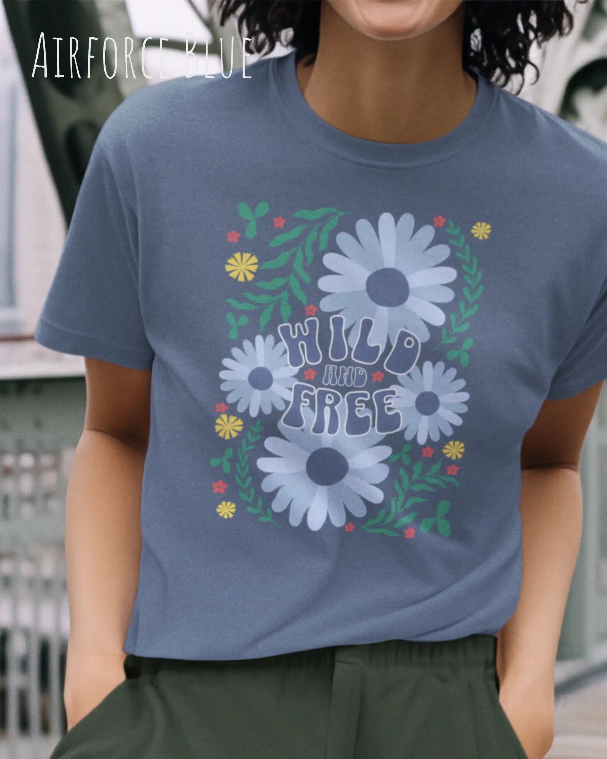 Das Bild zeigt eine Frau, die ein Design-T-Shirt in der farbe airforce blue  aus atmungsaktiver Baumwolle  mit dem statement WILD AND FREE trägt.