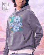 Eine Frau trägt den unisex Oversized Design-Hoodie JH111 von awdis in der Farbe dusty lilac mit dem STATEMENT Design WILD AND FREE.
