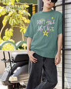 JUNGER Mann trägt das Heavyweight Oversized T-Shirt AWDis 240 T in der Farbe MOSS GREEN mit dem STATEMENT Design DON’T TALK JUST ACT