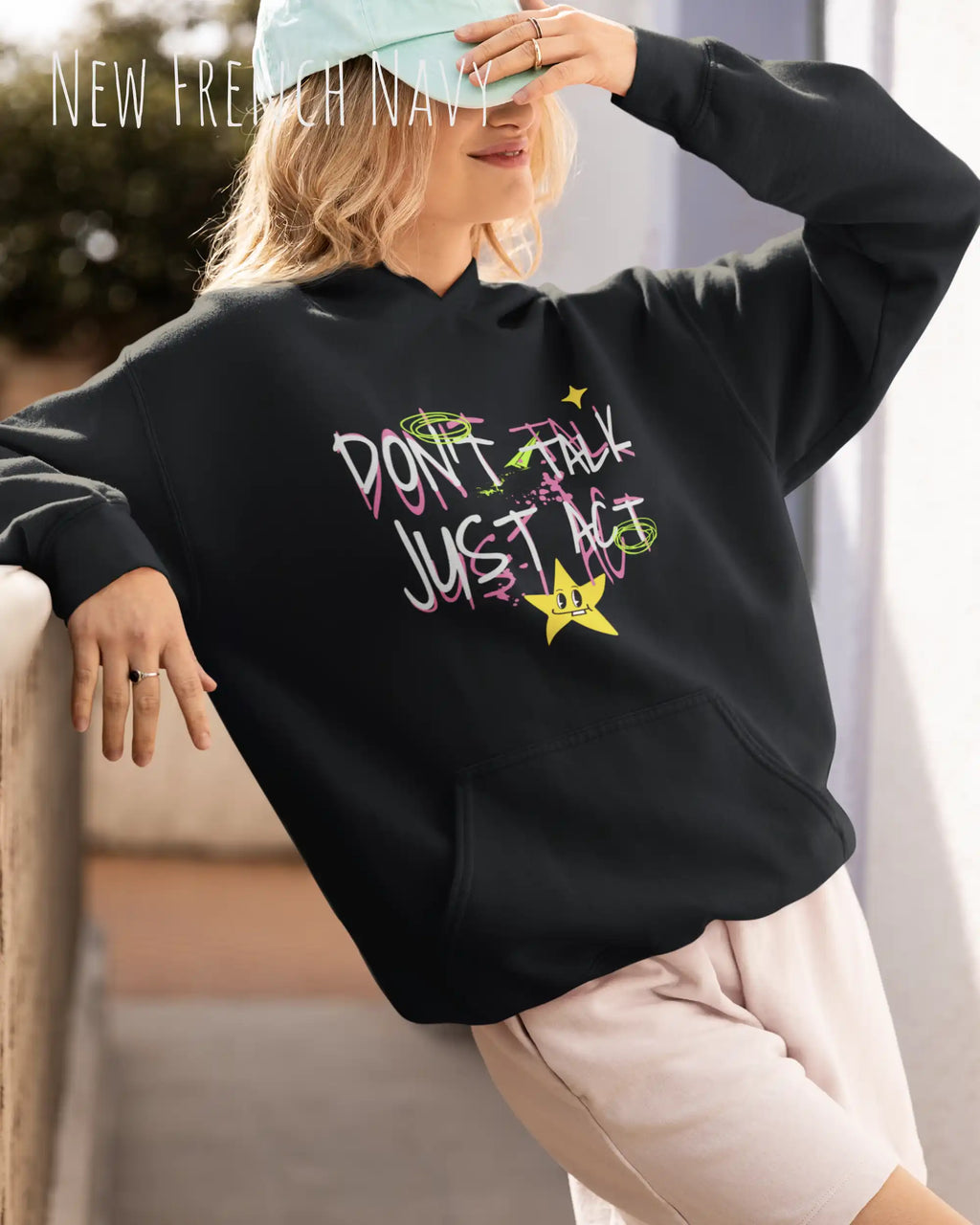 Eine blonde frau trägt einen oversized design hoodie in der farbe new French navy mit dem statement don't talk just act.
