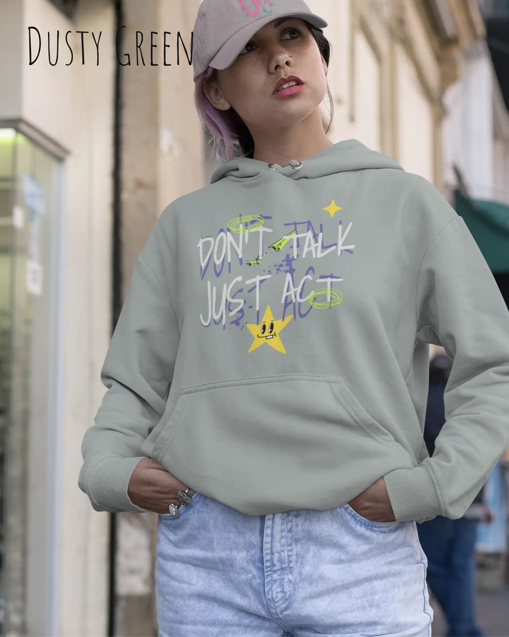 EINE junge FRAU mit basecap tRÄGT einen design hoodie in der Farbe dusty green mit dem STATEMENT don't talk just act,
