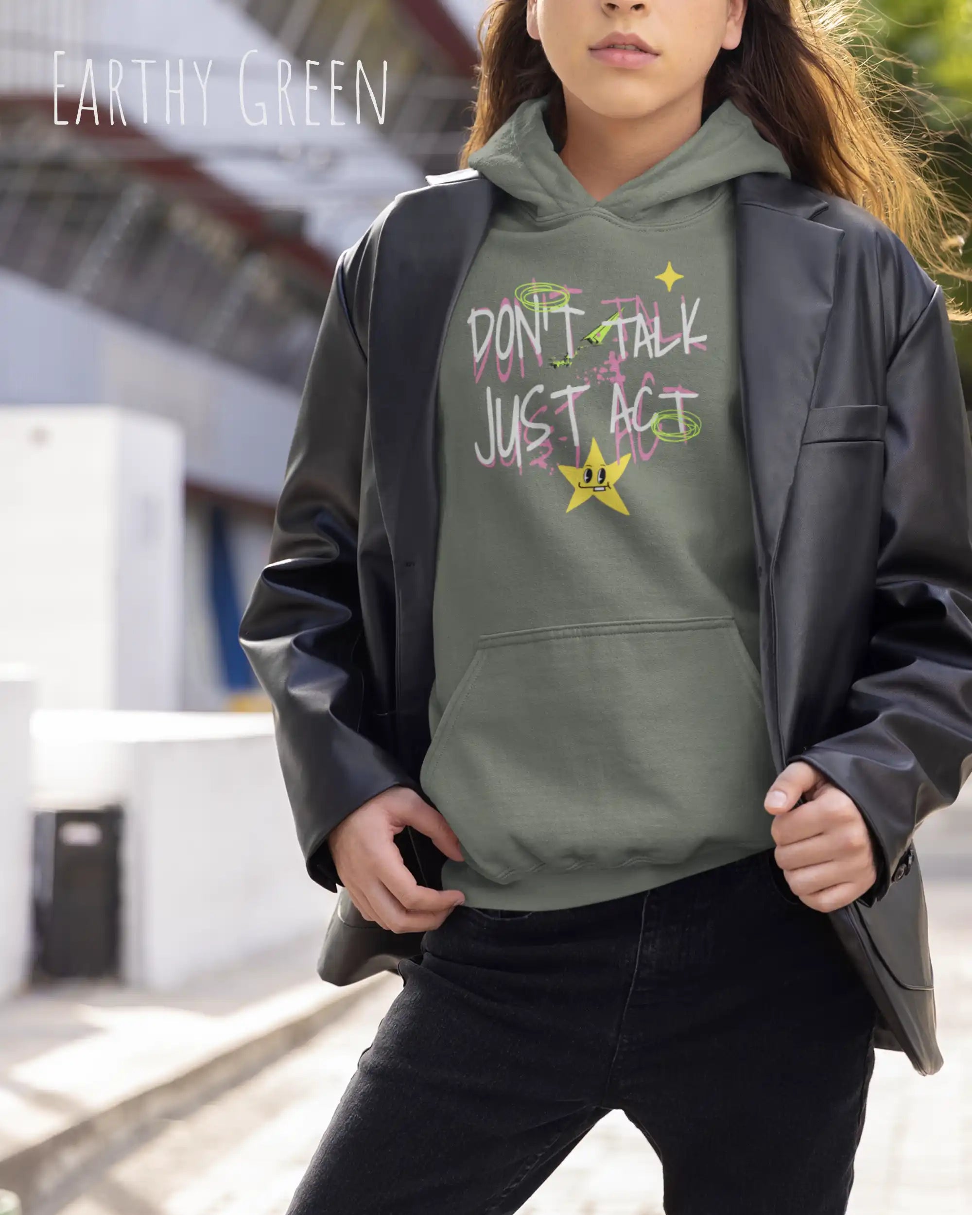 EINE FRAU mit Jacke TRÄGT einen design hoodie in der Farbe dusty green mit dem STATEMENT don't talk just act,
