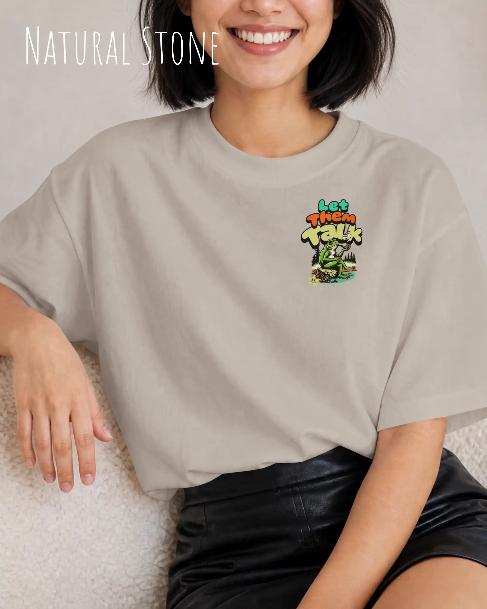eine frau trägt ein oversized heavyweight design-t-shirt in der farbe natural stone  mit dem entspannten motiv let them talk - lass sie reden – oben links.