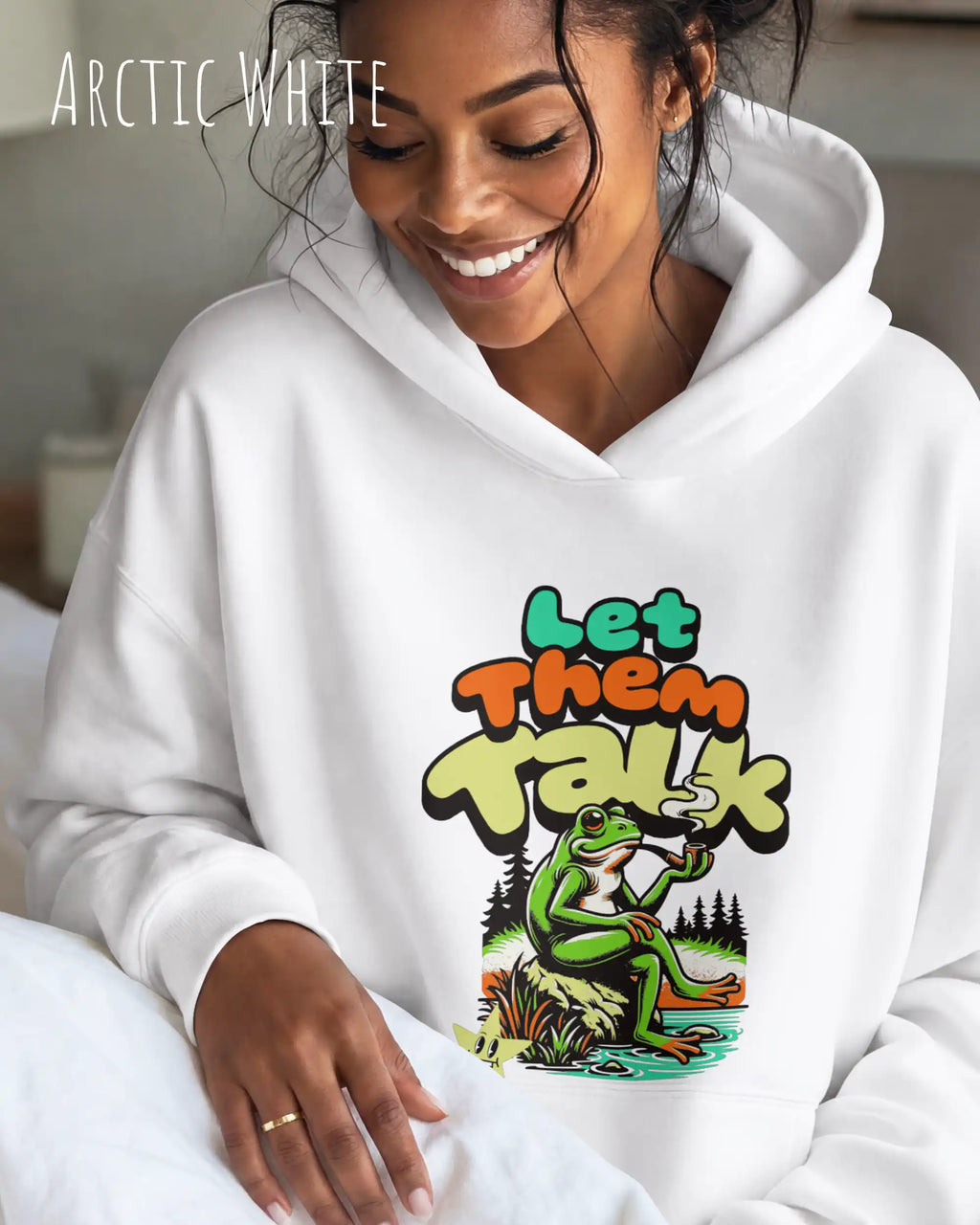 die Abbildung zeigt eine lächelnde frau, die einen Oversized Design-Hoodie in der farbe arctic white und mit dem humorvollen motiv "let them talk" trägt.