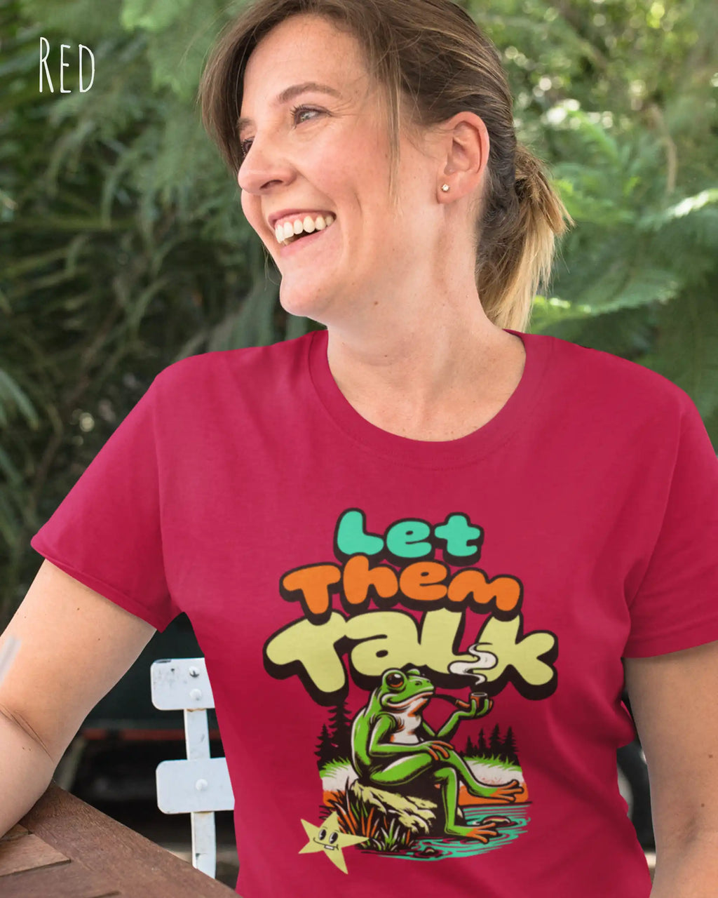 Dieses Bild zeigt eine fröhliche frau, die ein feminines design-t-shirt in der farbe red mit dem humorvollen design "LET THEM TALK" trägt.