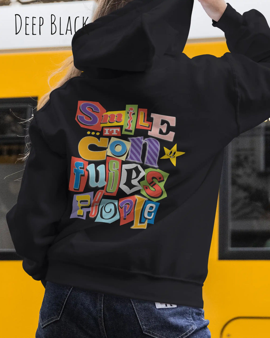 eine frau trägt einen Oversized Design-Hoodie JH111 in  deep black  mit der farbenfrohen grafik "Smile ... it confuses people" auf dem rücken.