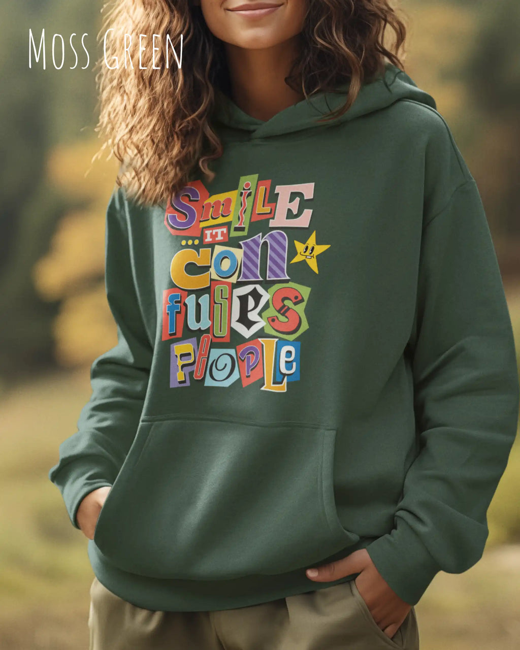 eine frau trägt einen Oversized Design-Hoodie in  moss green mit der farbenfrohen grafik "Smile ... it confuses people".