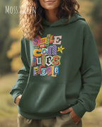 eine frau trägt einen Oversized Design-Hoodie in  moss green mit der farbenfrohen grafik "Smile ... it confuses people".
