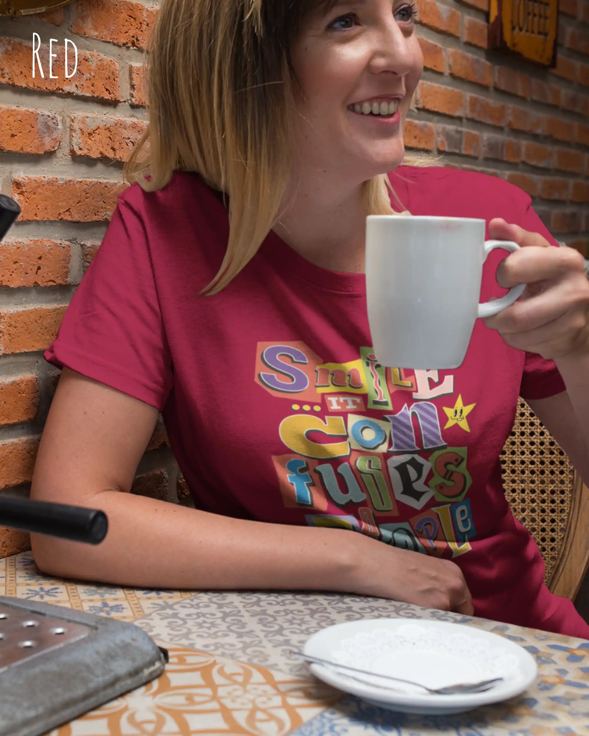 Frau im cafe trägt ein Design-T-Shirt  in red  mit dem frontprint "Smile, it confuses people".
