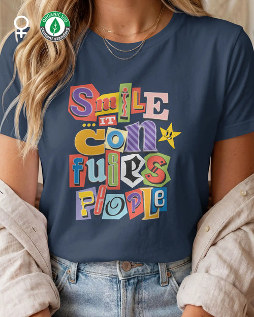 Die Abbildung zeigt eine blonde frau, die ein nachhaltiges design-t-shirt  mit femininem schnitt mit der farbenfrohen grafik "smile ... it confuses people" trägt.