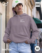 das bild zeigt eine junge frau, die einen unisex design hoodie in der farbe dusty lilac und mit dem minimalistischen motiv "less is more" trägt.