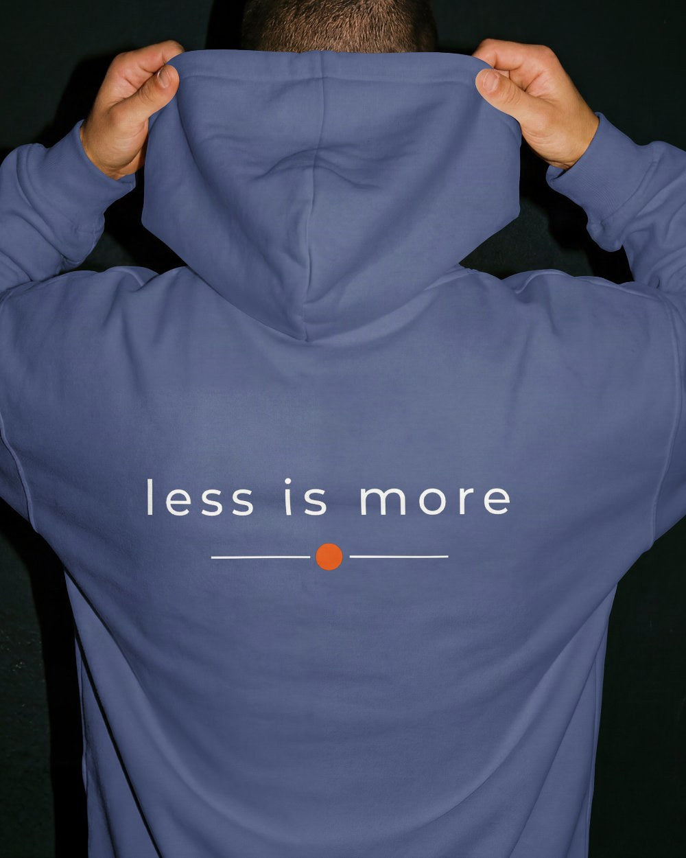 das bild zeigt eine person, die einen unisex design hoodie in der farbe denim blue und mit dem zeitlosen backprint "less is more" trägt.