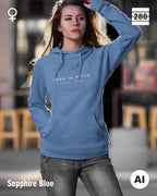 das bild zeigt eine frau, die einen leicht taillierten damen hoodie in der farbe sapphire blue und mit dem zeitlosen design "less is more" trägt.