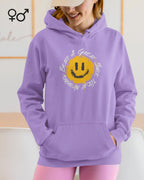 Eine lächelnde  junge frau trägt einen  unisex design-hoodie mit einem fröhlichen smiley-motiv.