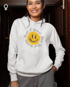 Eine lachende junge frau trägt einen femininen  design-hoodie mit einem fröhlichen smiley-motiv.